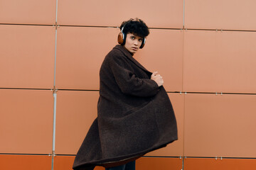 Fashionable young man in a coat and headphones standing against orange and red walls
