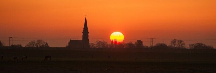 Fototapeta premium Silhouette of a country church at sunst with a big sun