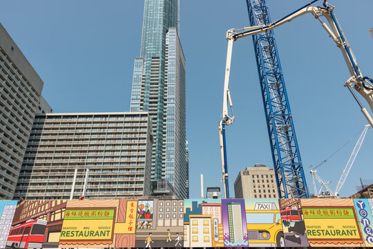 colorful hoarding banner with active construction site (8 Elm Street Condos), featuring concrete pump and crane, old buildings, and a recent skyscraper in Toronto, Canada