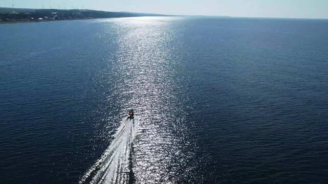 Un drone poursuit une chaloupe a moteur naviguant rapidement au travers les vagues soumissent aux reflets du soleil sur une ocean calme se fondant avec l'horizon.