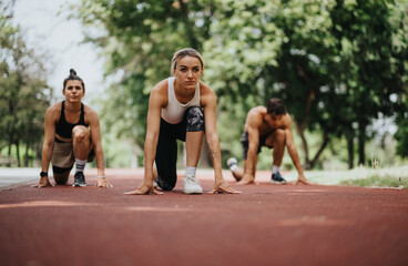 Group of young athletes in starting blocks preparing for a race on a sunny day on an outdoor running track.