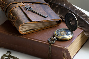 A close up image of two very old books stacked on a old office desk with a pocket watch and quill. 