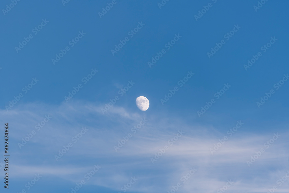 Wall mural a serene moon captured in a blue daytime sky with soft clouds, conveying calm and peace.
