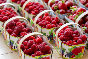 Baskets of fresh sweet organic red strawberries and raspberries for sale at a supermarket. The ripe...