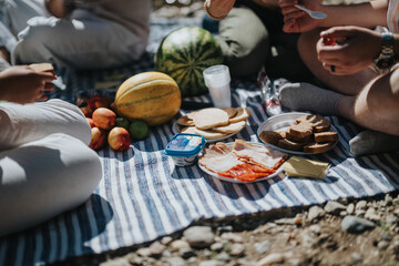 A group of friends gather for a relaxed summer picnic, sharing fresh fruits, sandwiches, and cheese on a blanket outdoors, creating a joyful and memorable experience in nature.