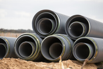 A stack of grey ribbed or corrugated industrial heavy PVC underground sanitary sewage pipes at a...