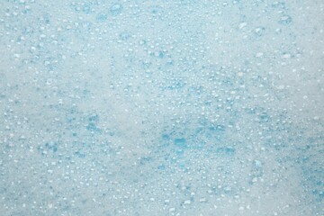 Washing laundry. White foam with bubbles on light blue background, top view