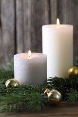 Burning candles, baubles and fir branches on wooden table, closeup. Christmas atmosphere