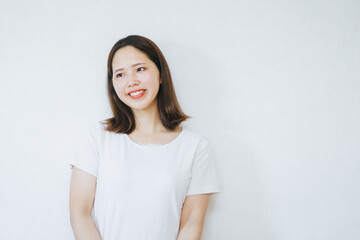 Obraz premium 白い壁の前で笑顔でいる女性 A woman smiling in front of a white wall