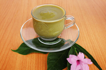 Smooth avocado juice in a glass cup with saucer, placed over leaves and pink flowers. on the brown wooden table

