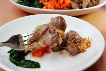 Use a fork to lift the pork into the sauce.  From a plate with carrots Fried garlic and green vegetables on a wooden table

