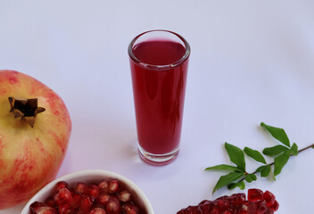 Dark red pomegranate juice in a glass placed in the center. Fruits, seeds and leaves on a white background.


