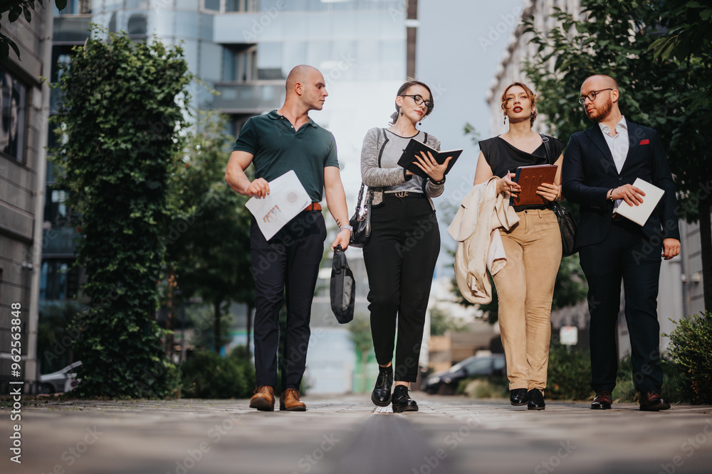 Wall mural A group of young professionals walking and discussing business outdoors in a modern urban environment. They appear engaged and focused.