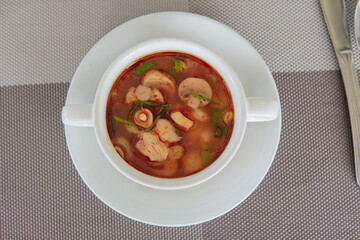 A bowl of tom yum soup, traditional hot and sour Thai soups with mushrooms, greens, and meat.