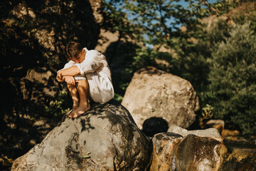 Man sitting alone on a rock in nature, deep in thought. Reflecting on life in a serene outdoor...