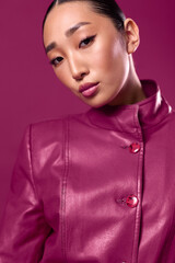 Fashionable asian brunette woman in a purple leather jacket posing with her eyes closed against a matching background, her hair in a ponytail