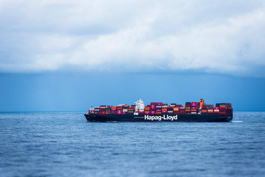 Fully loaded cargo container ship, owned by the Hapag-Lloyd company, sailing through calm, blue ocean. 