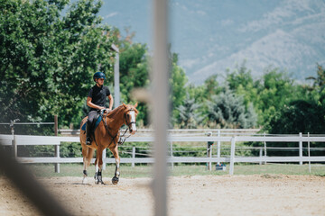A young rider is seen on horseback in an outdoor equestrian center, enjoying a sunny day with...