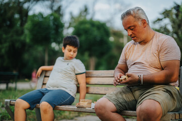 Fototapeta premium A father and son enjoy quality time together playing with building blocks on a park bench, fostering creativity and bonding.