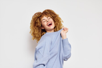 Happy woman with curly hair smiling joyfully in light blue sweater against plain white background, expressing happiness and positivity, perfect for cheerful content