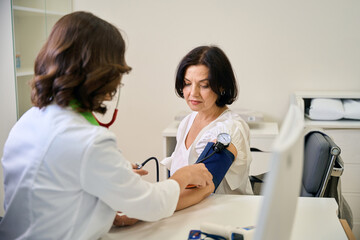 Clinic employee at reception measures blood pressure of middle-aged patient