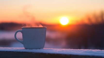 A steaming cup of hot drink sits on a snowy ledge as the sun rises, illuminating the winter landscape
