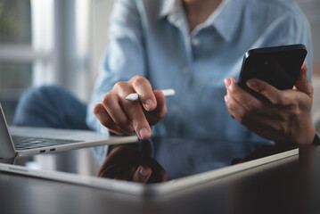 Young woman in casual wear online working from home office, using digital tablet, mobile phone and...