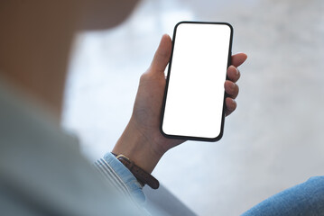 Mockup, woman's hands holding mobile phone with blank screen in coffee shop, over shoulder view