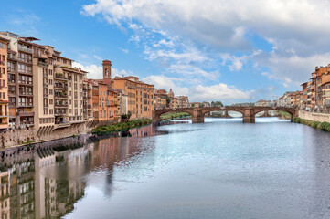 Obraz premium View of the Arno River and Santa Trinita Bridge in Florence with historical architecture lining the banks and a clear blue sky above