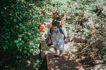 A young man with a backpack climbs steps in a lush forest. Captured from above, this scene depicts a vibrant summer hiking adventure full of exploration and nature.