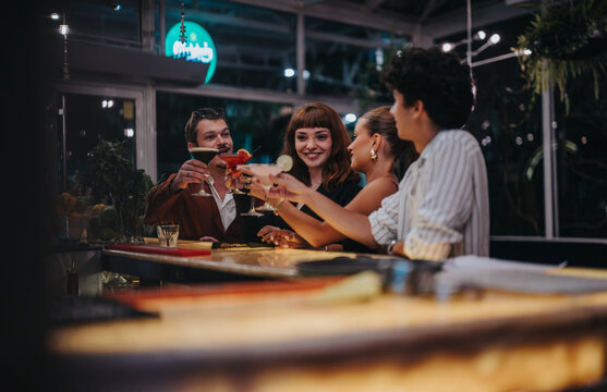 Group of friends socializing and raising cocktails at a stylish bar. They are smiling and enjoying a lively evening filled with laughter and good company.