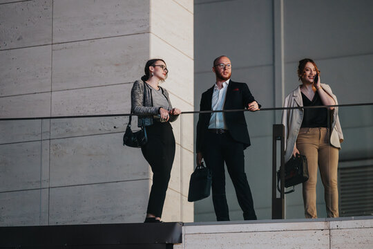 Three business professionals discuss and strategize on a modern balcony, showcasing teamwork and corporate collaboration.