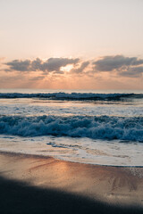 Golden sunrise over foamy waves reflecting on the sandy beach.