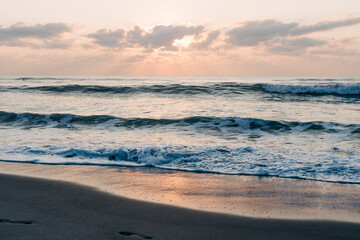 Golden sunrise on the shore with gentle waves and soft clouds
