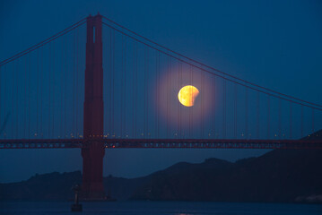 Lunar eclipse over the Golden Gate Bridge at night with a glowing moon