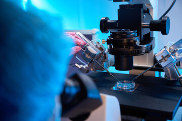 Lab technician adjusting micromanipulation tools under a microscope
