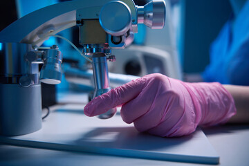 Hand operating a micromanipulator next to a microscope