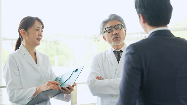 ビジネスマンから説明を受ける白衣の医師・研究者