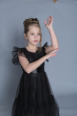 A young dancer in a black ruffled dress extends her arm, moving with grace and elegance. This image...