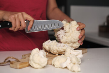 A person skillfully chopping cauliflower with a knife, capturing the essence of food preparation. The photo emphasizes the value of using fresh, wholesome ingredients in everyday meals.