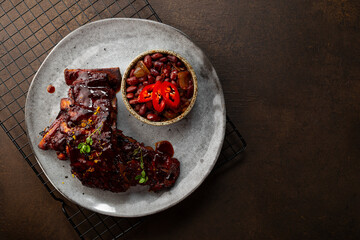 Roasted Pork Ribs in BBQ Sauce with Red Beans in the plate and dark background top view copy space for text