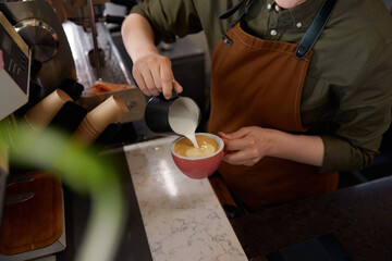 View form above on barista hands pouring milk into coffee in cup