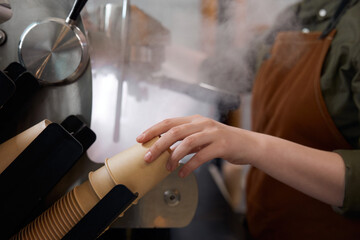Closeup female barista taking paper coffee cup while preparing coffee