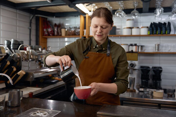 Barista hands pouring milk into coffee in cup
