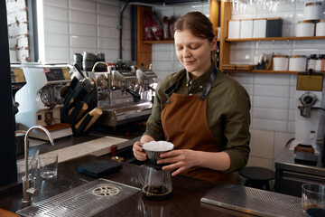 Young woman barista using stainless steel funnel for coffee filtration