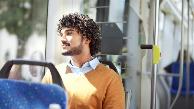 Young handsome man riding public transport while looking out window, reflecting urban lifestyle and daily commute looking at window in bus while traveling in city