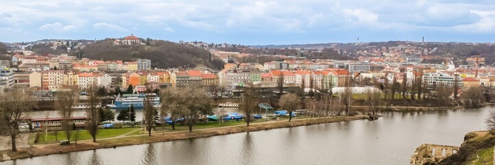 Obraz premium Panoramic view of Prague's colorful riverfront buildings and hills during early spring, highlighting urban tourism and scenic travel