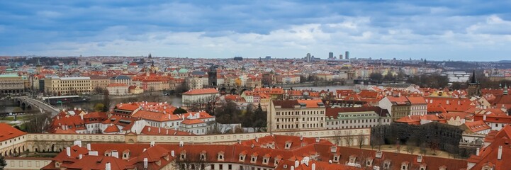 Panoramic view of Prague's historic cityscape with traditional red rooftops under cloudy skies, capturing European urban charm and architecture