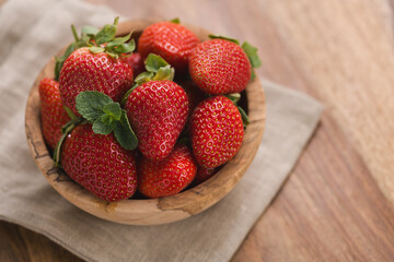 Ripe strawberries in wooden bowl on wood background with copy space