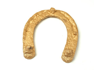 A gold horseshoe is shown on a white background. The horseshoe is curved and has a shiny, metallic...